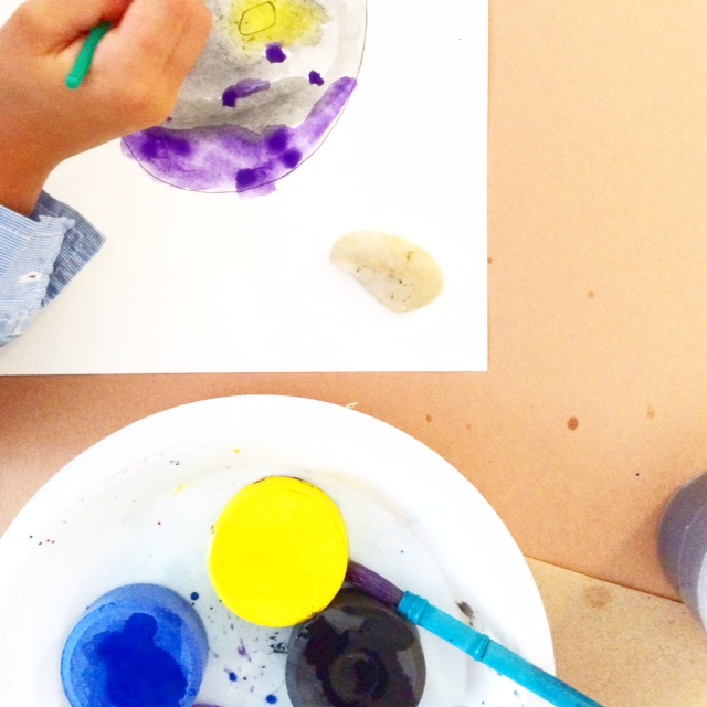 Child painting a purple and yellow rock with paintbrush.